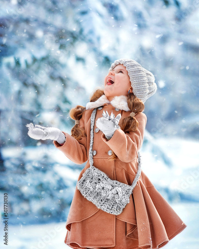 Portrait of happy cheerful girl kid in winter in the park catches snowflakes with her mouth tongue, enjoying winter in the park.