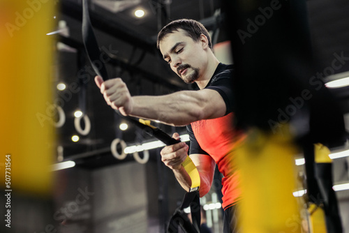 Sports background. Man training with fitness straps in the gym. 