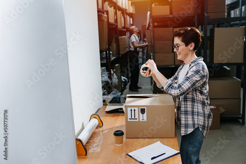 Short haired female warehouse worker in good spirits packing a cardboard box