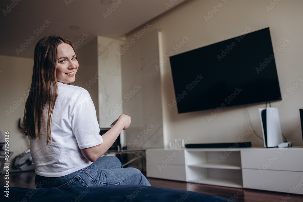 Young Woman Sitting On Couch Watching Movie On Television At Home