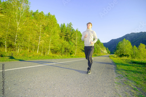 Running man jogging in city park at beautiful summer day. Sport fitness model caucasian ethnicity training outdoor.