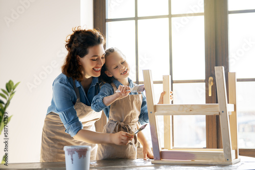 Photography mother and daughter are painting a wooden stool