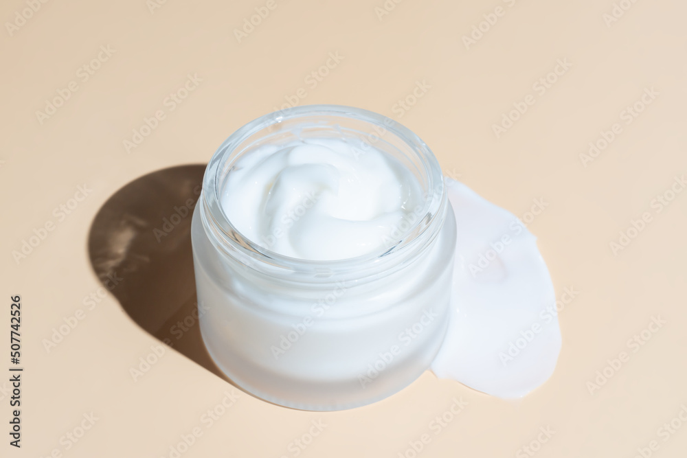 Frosted glass jar of moisturizer cream on beigebackground. Natural eco-friendly beauty product branding, packaging design. Cream smear texture Frosted glass jar of moisturizer cream on beigebackground. Natural eco-friendly beauty product branding, packaging design. Cream smear texture