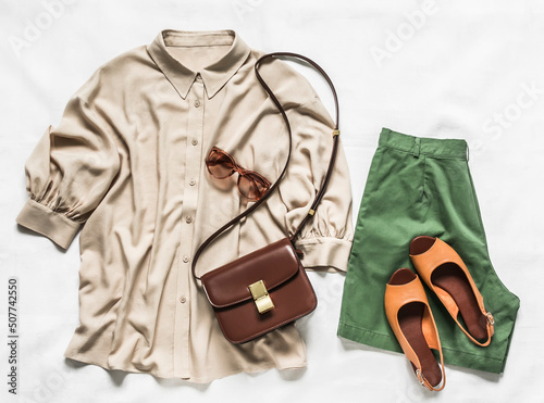 Women's clothing - viscose blouse, cotton bermuda shorts, leather sandals and cross body bag on a light background, top view