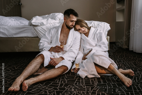 Happy young couple sitting on the floor near the bed in hotel with glasses of champagne photo