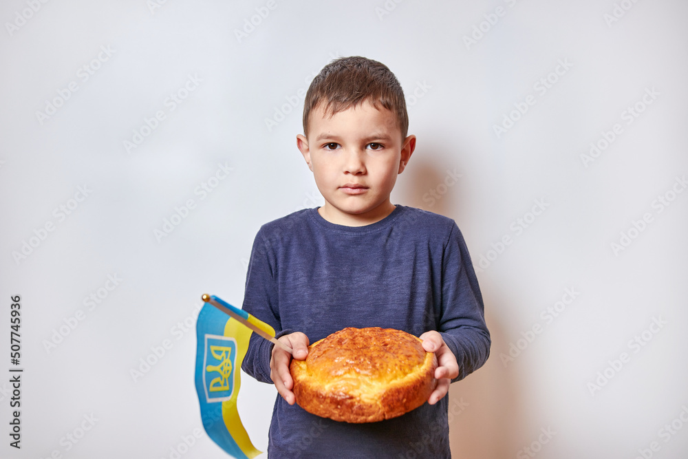 The boy holds freshly baked bread and the flag of Ukraine. The threat of growing bread in Ukraine due to the war. The boy holds freshly baked bread and the flag of Ukraine. The threat of growing bread in Ukraine due to the war.