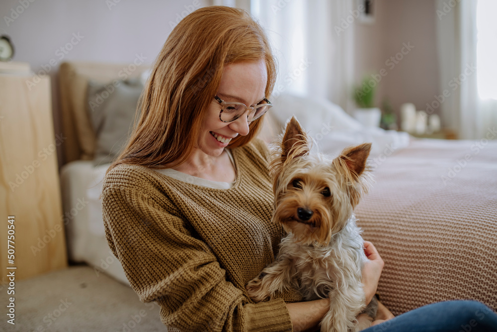Happy woman with pet dog sitting by bed at home Happy woman with pet dog sitting by bed at home