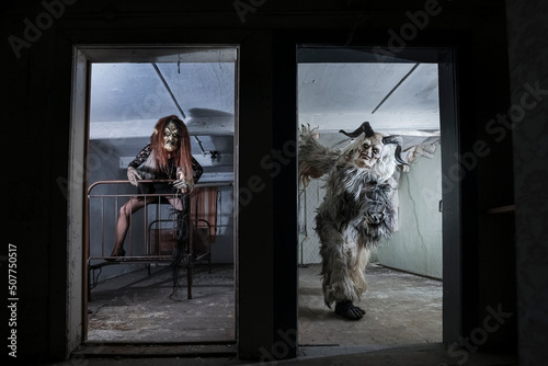 Man and woman in spooky costumes seen through door at horror house photo