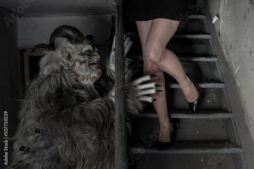 Man in krampus costume trying to scare woman moving down on steps at horror house