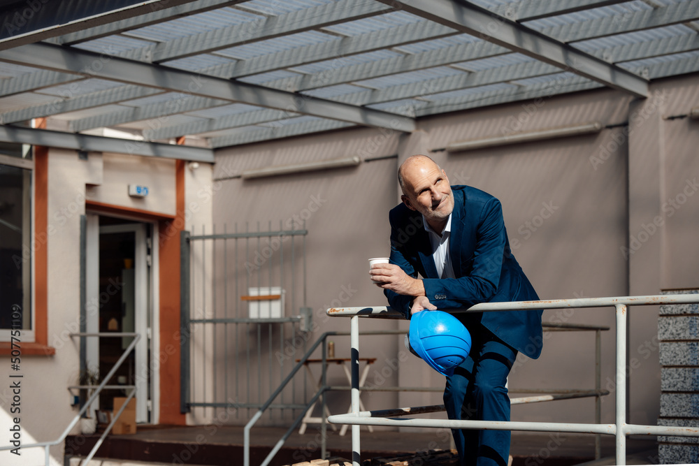 Businessman holding hardhat and cup standing at construction site Businessman holding hardhat and cup standing at construction site