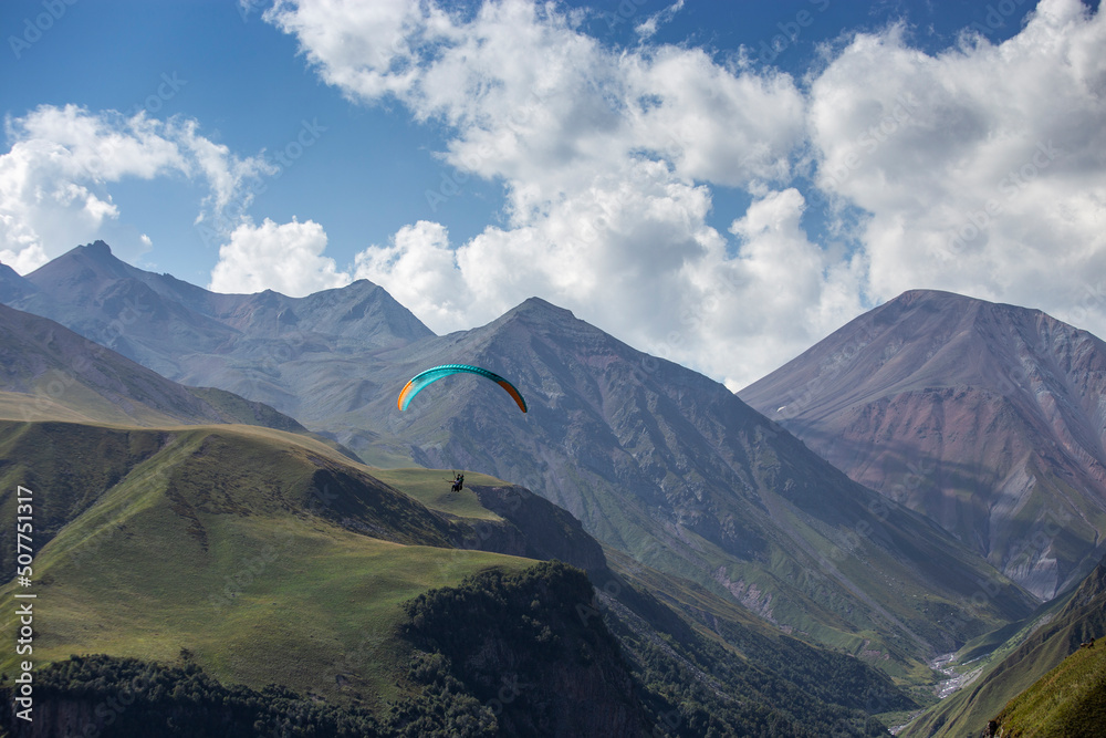 A man on a paraglider takes a selfie. Mountain gorge with green slopes