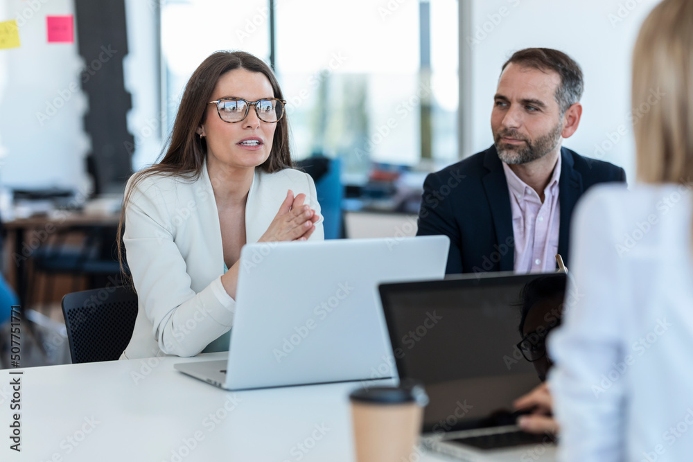 Businesswoman wearing eyeglasses discussing strategy with colleagues in office Businesswoman wearing eyeglasses discussing strategy with colleagues in office