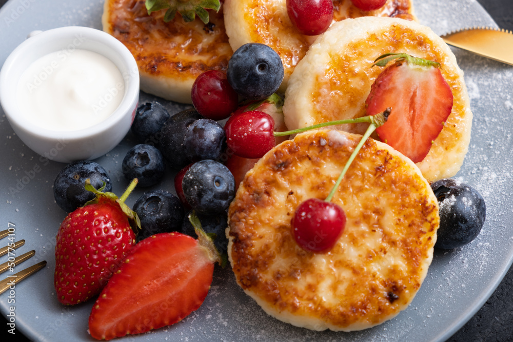 Close-up roasted cheesecakes on a plate with powdered sugar and berries angle view