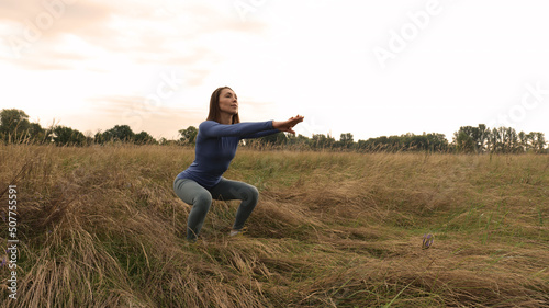 An Asian woman is training in a dry field. Sports woman squats in nature