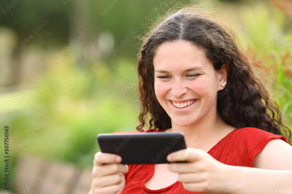 Happy woman in a park watching videos on smart phone