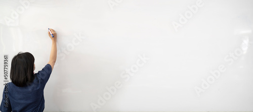Tableau sur toile Woman in white shirt writing on imaginary screen whiteboard with blue marker on white background