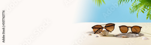 Sunglasses fashion offer banner. Summer sunglass sale-out offer. Sunglasses on a beach sand with tropical leaves. Summer Optics store web line. Copy space  side view. Trendy accessories
