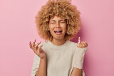 Frustrated doleful woman with curly hair wears bandage on injured arm and plaster cries and feels pain dressed in casual t shirt has health problems isolated over pink background. Painful feelings