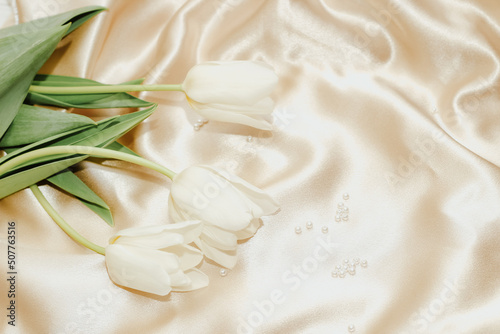 Bouquet of white tulips with pearl beads on silk golden nude satin background.