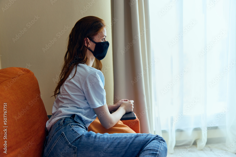 woman sitting on the orange sofa at home in protective masks stay home concept woman sitting on the orange sofa at home in protective masks stay home concept