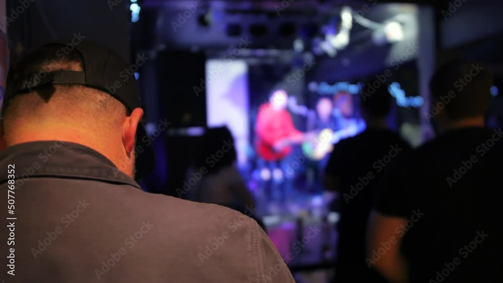 A distracted man texting on a phone while a band are playing on stage in a bar