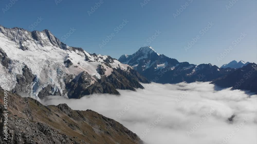 Pan over Mount Cook, New Zealand mountain range with big rocks and an amazing sea of clouds in the foreground and snow covered mountains in the background