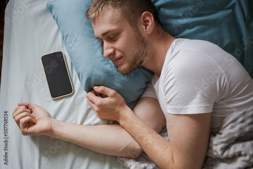 A man is asleep in bed with his phone next to him.