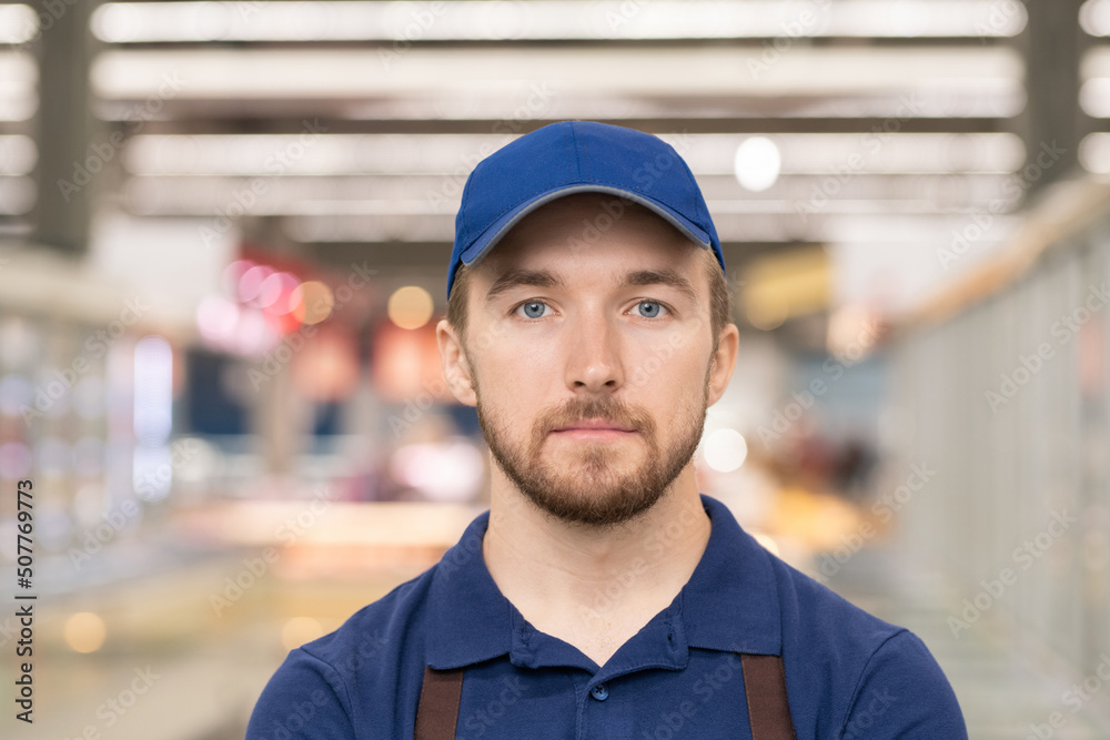 Head and shoulders portrait of handsome young man working in supermarket standing in aisle looking at camera Head and shoulders portrait of handsome young man working in supermarket standing in aisle looking at camera