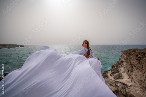 Happy freedom woman on the beach enjoying and posing in white dress. Rear view of a girl in a fluttering white dress in the wind. Holidays, holidays at sea. © svetograph