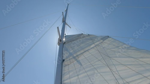 Raising the main sail of a sailing boat with the sun straight above the mast on a perfect blue sky  photo