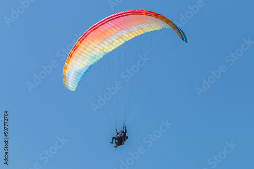 Multi-colored paraglider against the blue sky. Tandem flight.