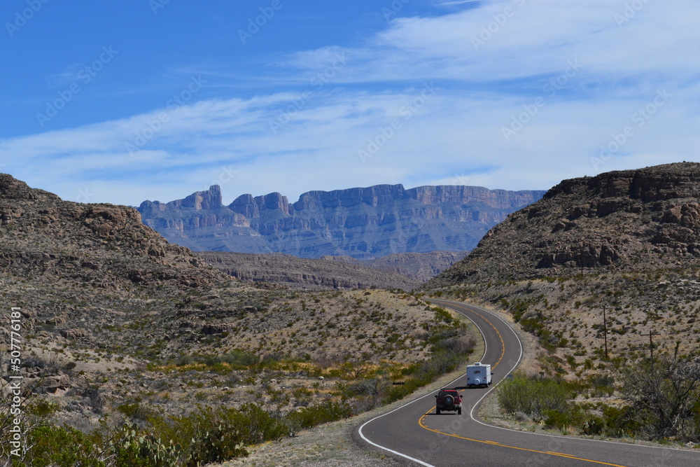 Eine Straße mit zwei Autos schlängelt sich durch die Berge und Wüste mitten im Big Bend National Park in Texas, Vereinigte Staaten von Amerika.