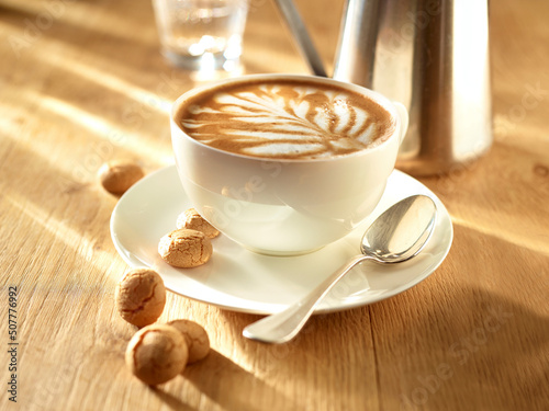 Milchkaffee mit Milchschaummotiv und Amarettinis auf einem hellen Holzfond photo