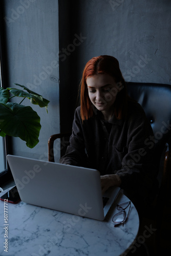 red-haired woman freelancer works remotely on laptop in cafe.
