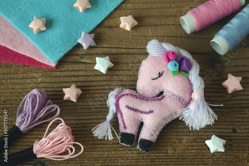 Making pink unicorn decored with purple and pink flower. Sewing from felt with your own hands. DIY concept for children. Handmade crafts.