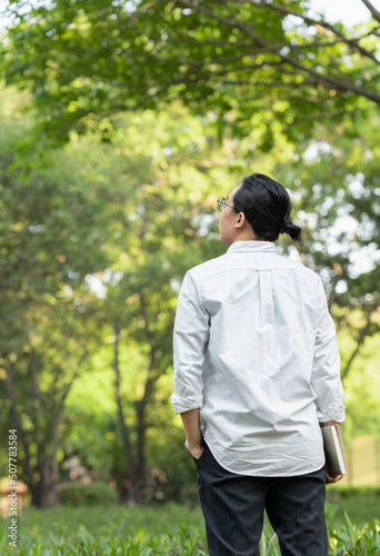 back view of an asian young man holding a book in the park 