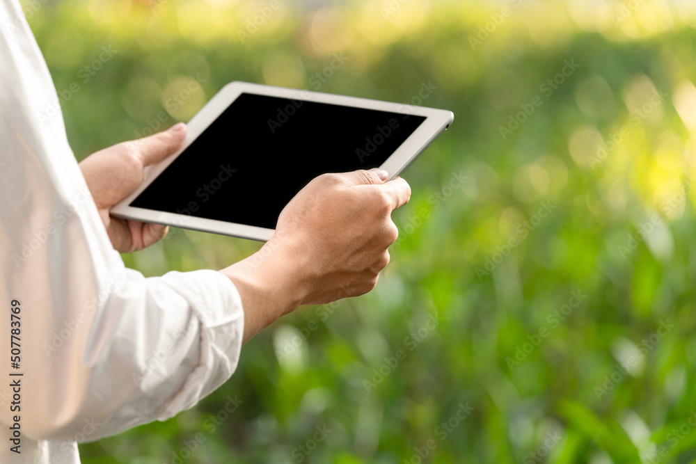 close up of hand holding tablet at outdoor green background 