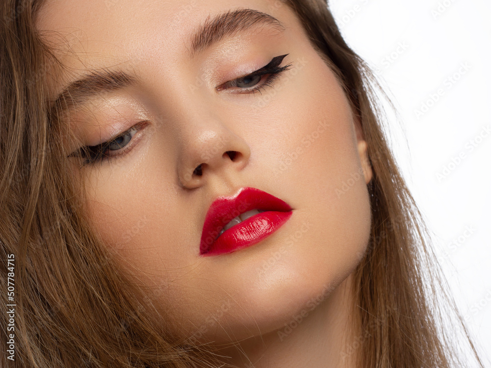 Fototapeta premium Close up portrait of a face with beautiful skin and evening makeup, eyeliner and long eyelashes, puffy red lips and white flowers. Fashion photography. Cosmetology and spa. Freshness of spring
