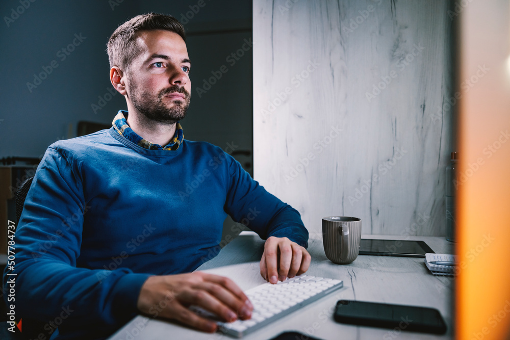 A businessman sitting in home office at night and working on computer.