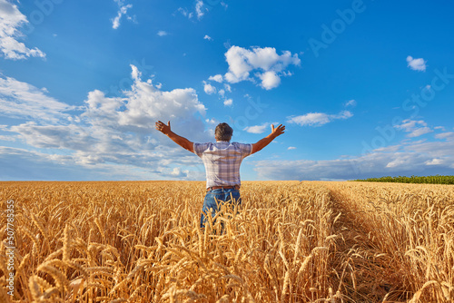 Happy farmer proudly standing in wheat field. Agronomist wearing corporate uniform, looking at camera on farmland. © Ryzhkov Oleksandr