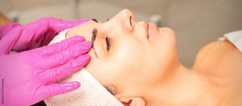 Cosmetologist with gloved hands applies a moisturizing mask with peeling cream on the female face. Facial cosmetology treatment. Procedures for facial care Cosmetologist with gloved hands applies a moisturizing mask with peeling cream on the female face. Facial cosmetology treatment. Procedures for facial care