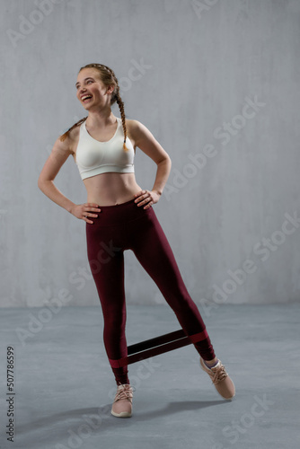 Sports woman in fashion sportswear exercising with elastic band stretch over greay background.