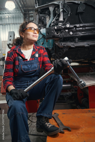 Woman auto mechanic holding car repair tool in garage