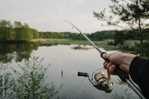 Fisherman with fishing rod, spinning reel on the background river bank. Sunrise. Fishing the backdrop of lake.