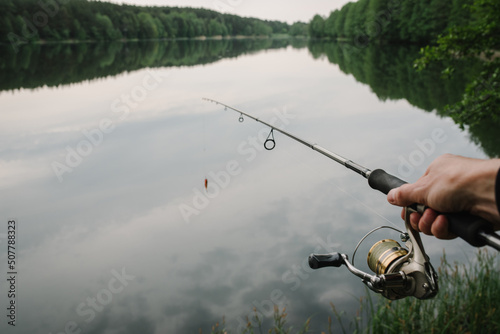 Fisherman with rod, spinning reel on the river bank. Fishing for pike, perch, carp. Fog against the backdrop of lake. background Misty morning. wild nature. The concept of a rural getaway.