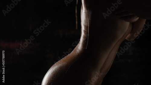Beautiful tanned body close-up on a black background. Milk is poured on the girl's body close-up.