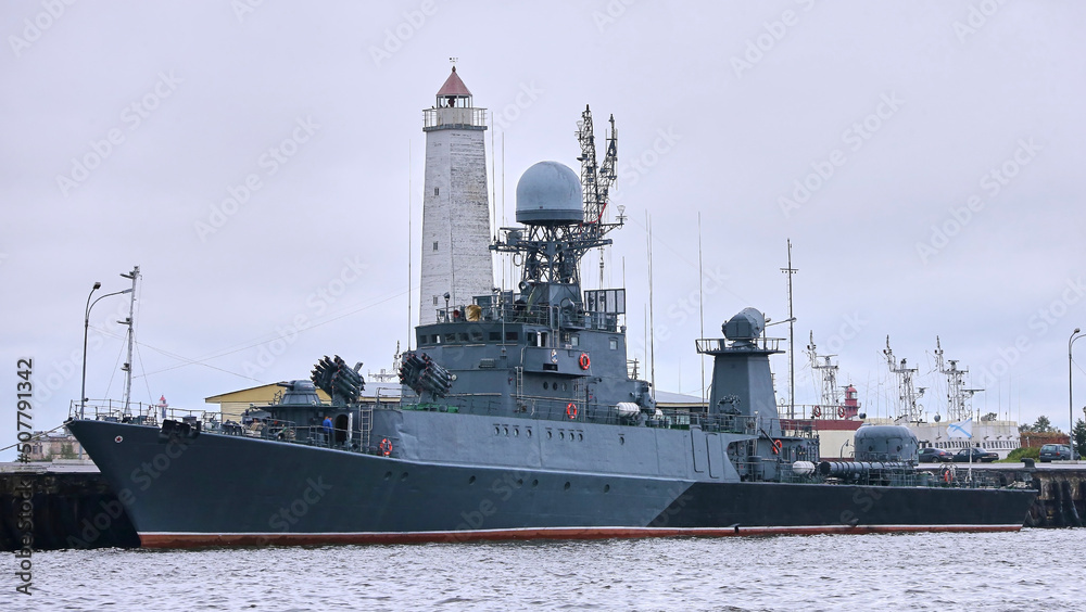 A large missile boat of the Russian Navy is moored near the lighthouse.