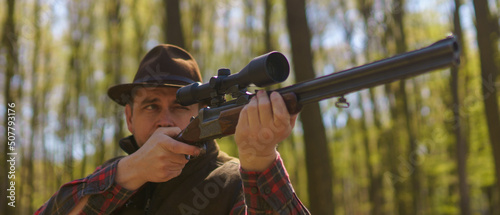 Obraz na płótnie Hunter man aiming with rifle gun on prey in forest.