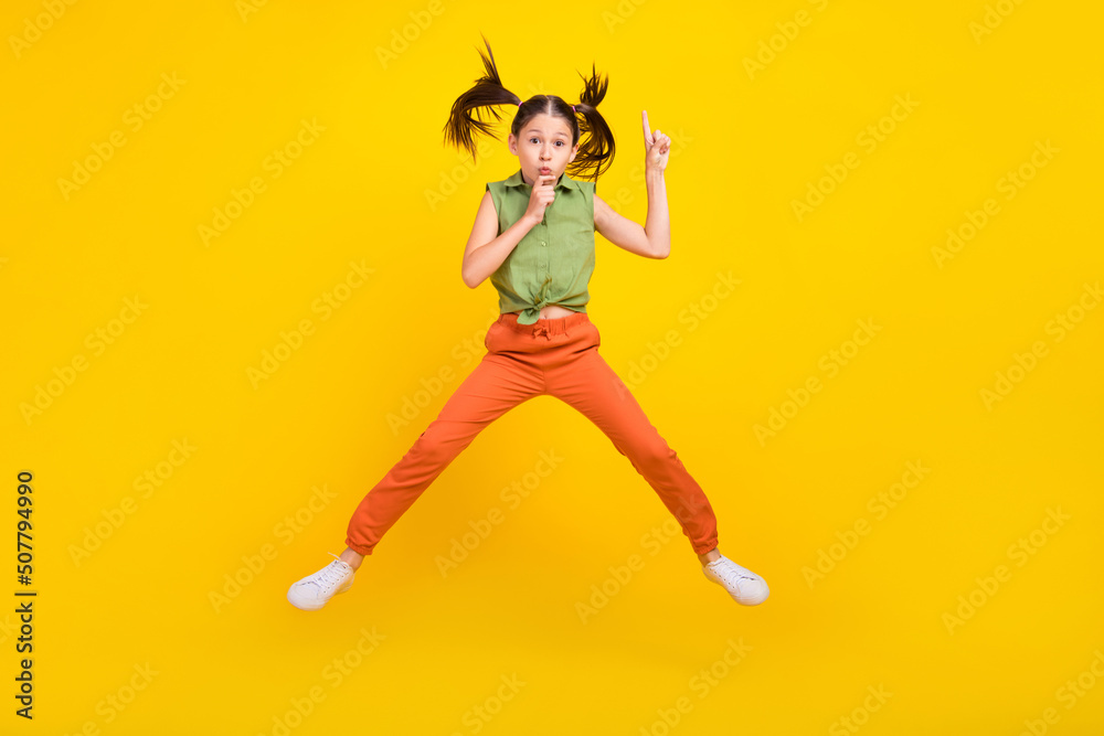Photo of shiny serious student girl wear green shirt smiling jumping high finger lips asking keeping silence isolated yellow color background