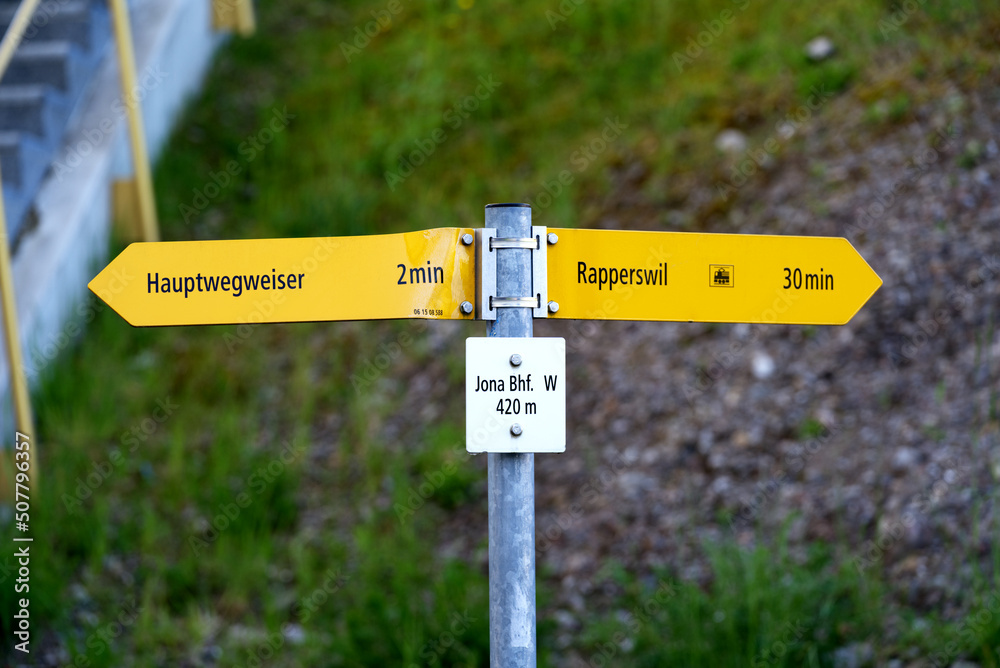 Yellow direction sign of hiking trails at City of Jona on a sunny spring day. Photo taken April 28th, 2022, Rapperswil-Jona, Switzerland.
